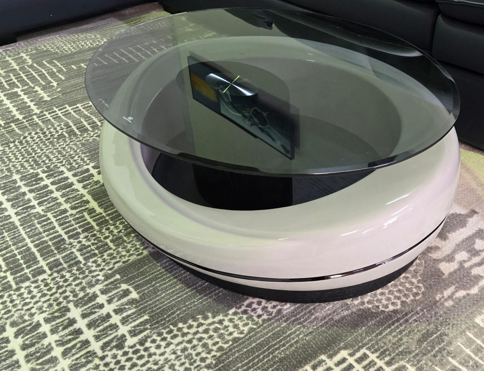 Round glass-top coffee table with white base on a textured surface